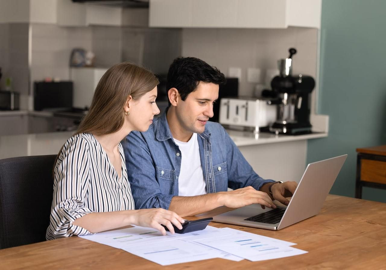 A man and a woman sitting at a table in front of a laptop, counting expenses.
